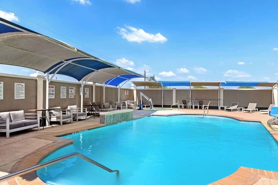 Resort swimming pool with retractable shade canopies and lounge chairs overlooking landscape