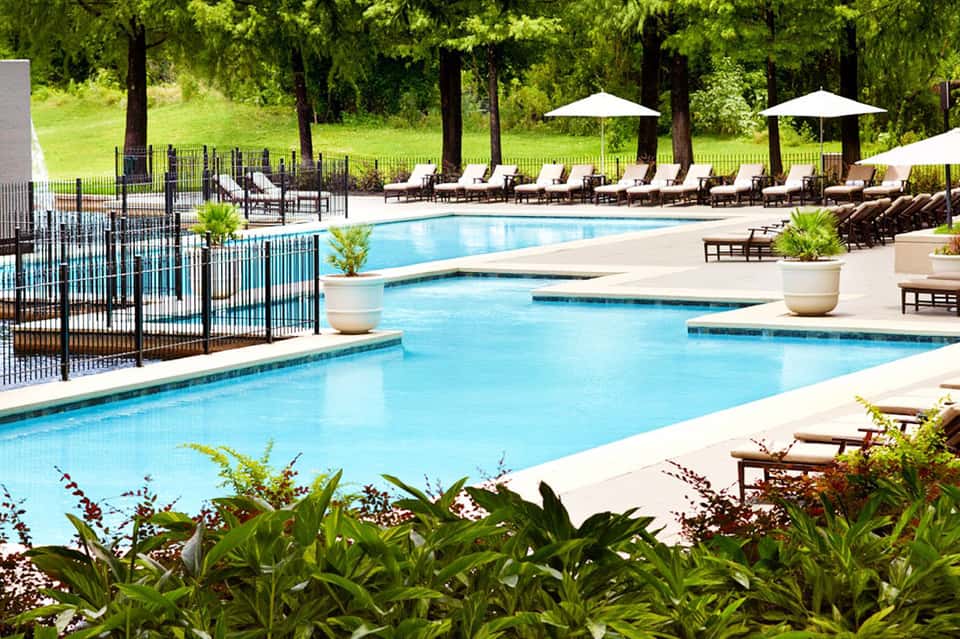Resort pool with lounge chairs and white umbrellas surrounded by manicured lawns and forested landscape