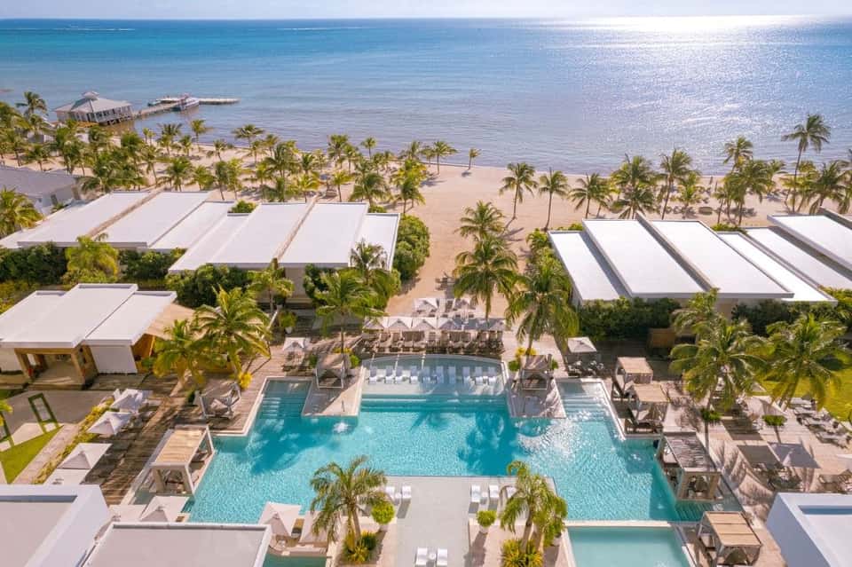 Aerial view of beachfront resort with pools, white cabanas, palm trees, and pristine sandy beach