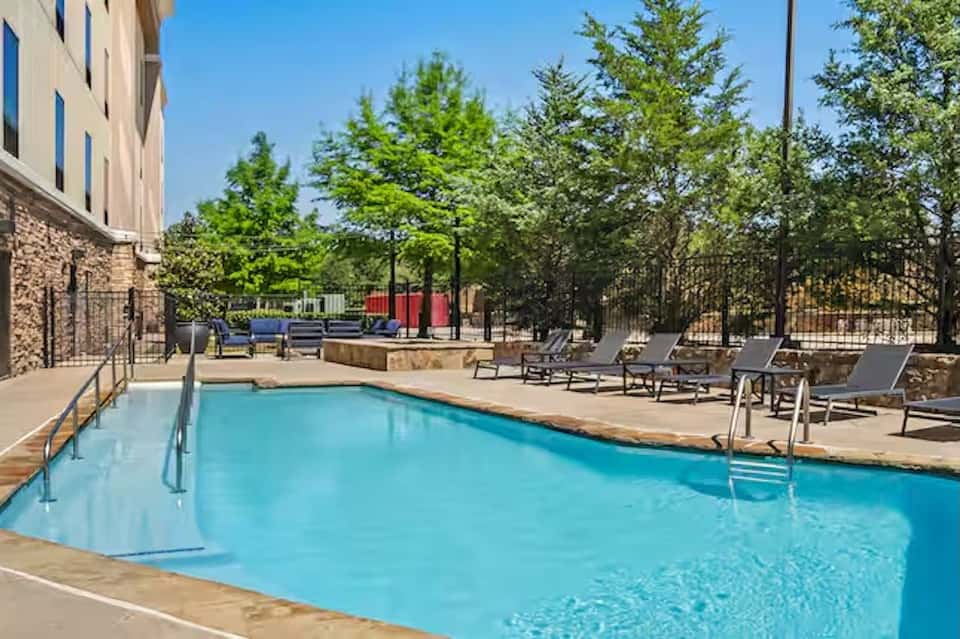 Resort pool with stone deck, lounge chairs, trees, and hotel building with brick exterior visible
