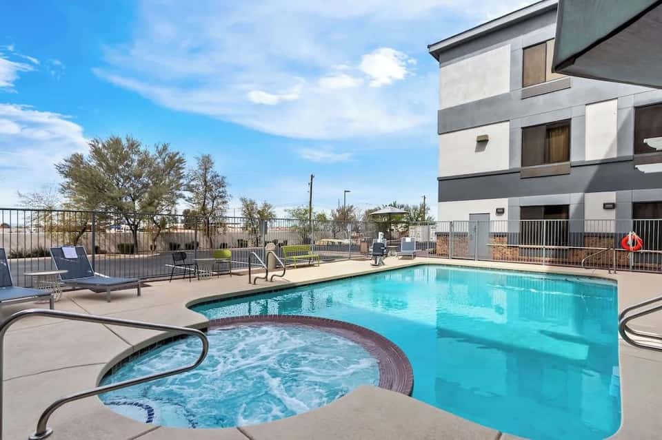 Heated pool and hot tub with desert landscaping, lounge seating, and modern hotel facade
