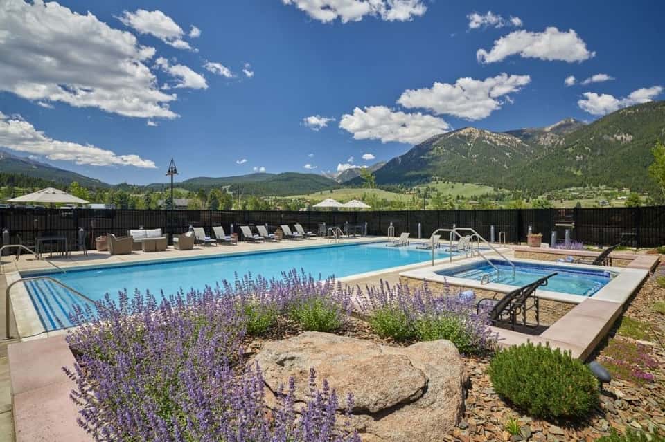 Resort pool with purple flowers, loungers, hot tub, and snow-capped mountain backdrop