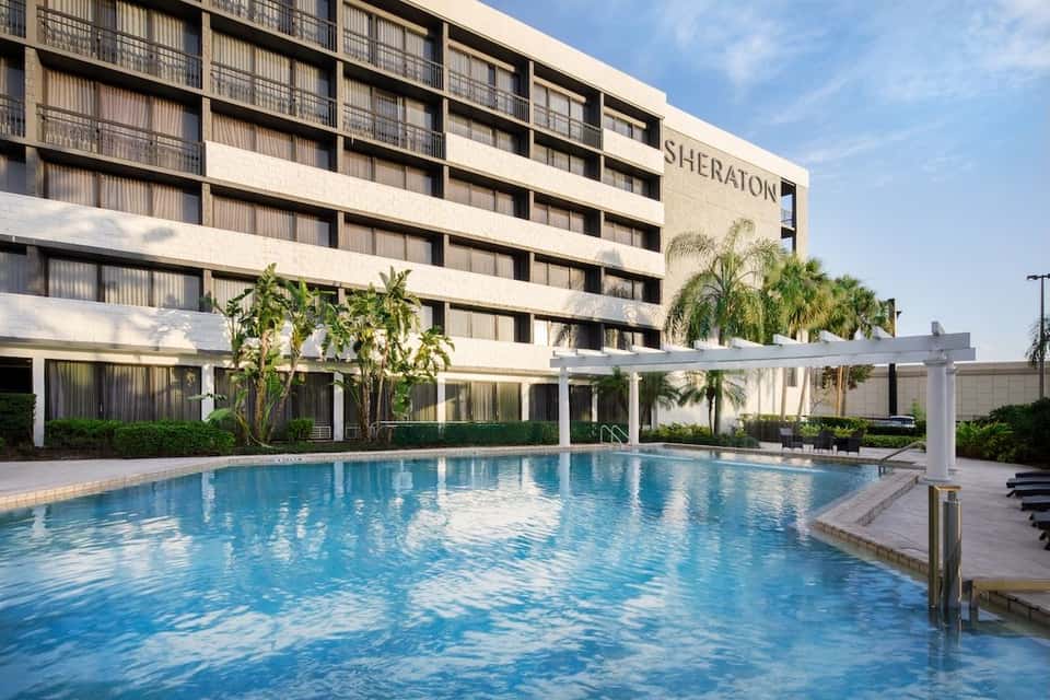 Sheraton hotel exterior with modern architecture, outdoor pool with shade structure, and manicured tropical grounds