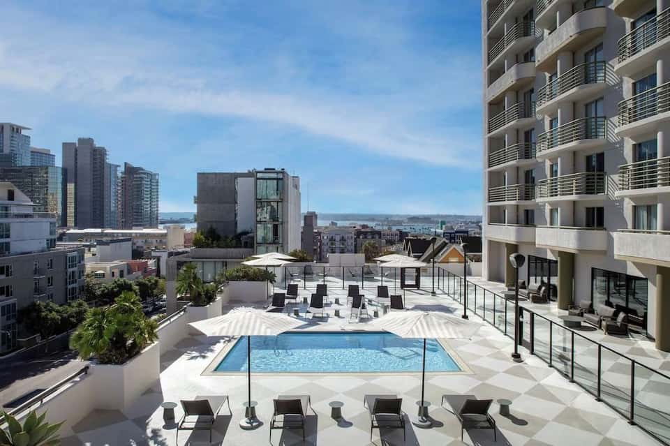 Rooftop pool deck with lounge chairs overlooking cityscape and waterfront during daytime