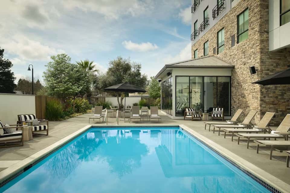 Resort swimming pool with crystal blue water, loungers, umbrellas, and brick building with patio seating area