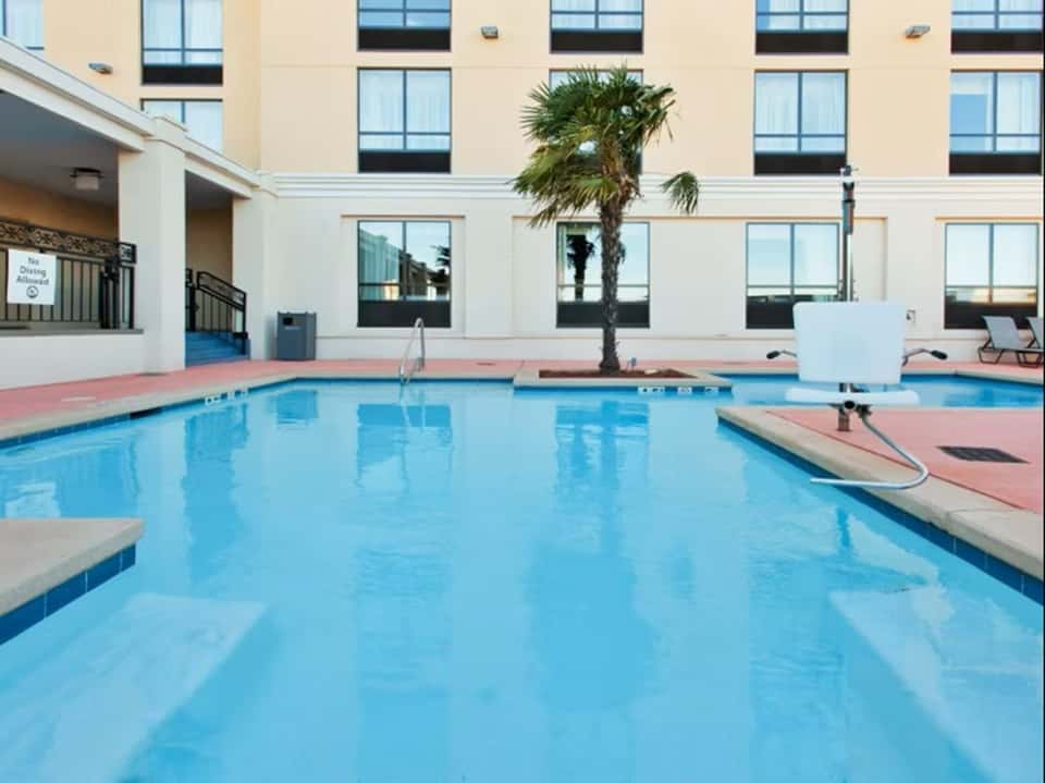 Indoor hotel pool with blue water, palm tree, and cream-colored building with multiple windows