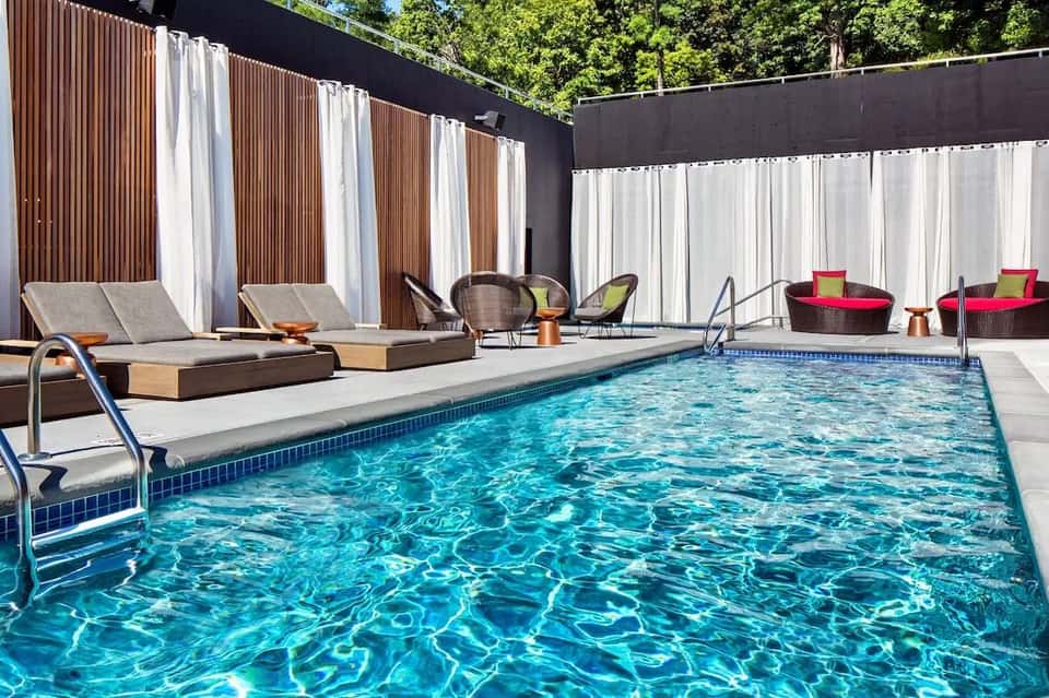 Resort pool deck with lounge chairs, striped cabanas, white umbrellas, and privacy screens