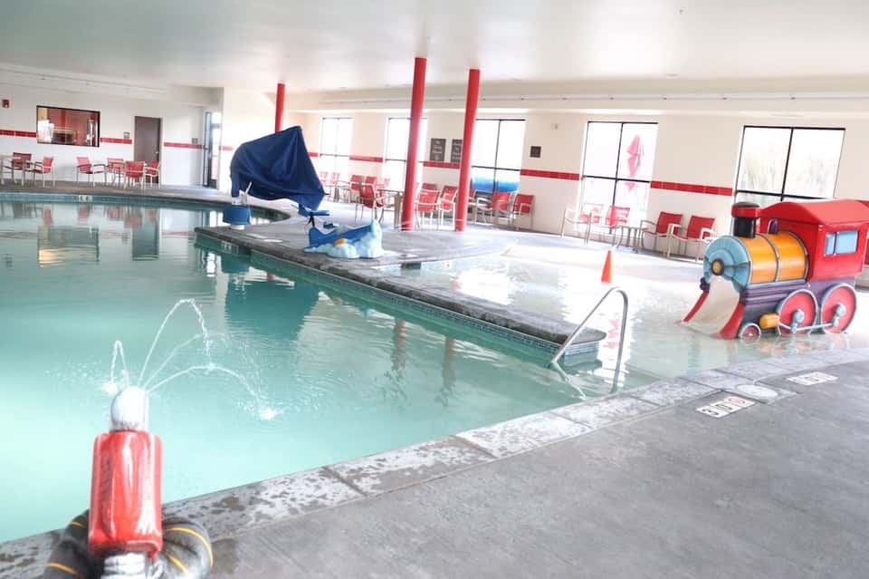 Indoor swimming pool with water features and red play equipment in brightly lit facility