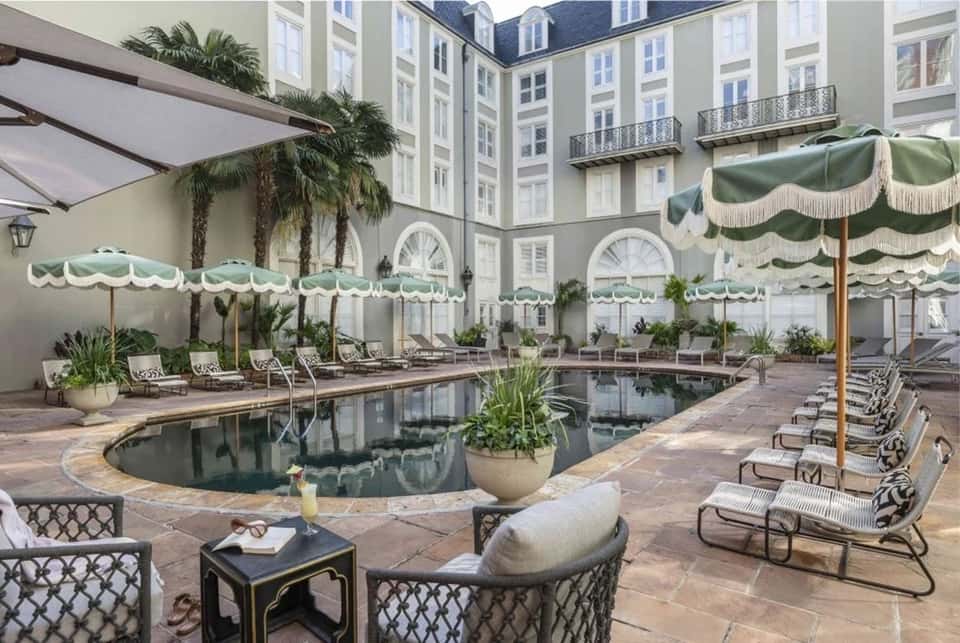 Elegant courtyard pool surrounded by upscale apartment buildings with green striped umbrellas and lounge seating