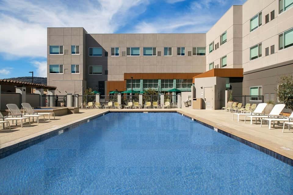 Resort outdoor swimming pool with loungers, green umbrellas, and modern multi-story building