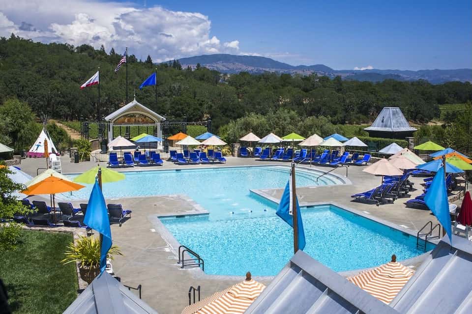 Resort pool area with multiple pools, blue loungers, colorful umbrellas, and mountain views in background