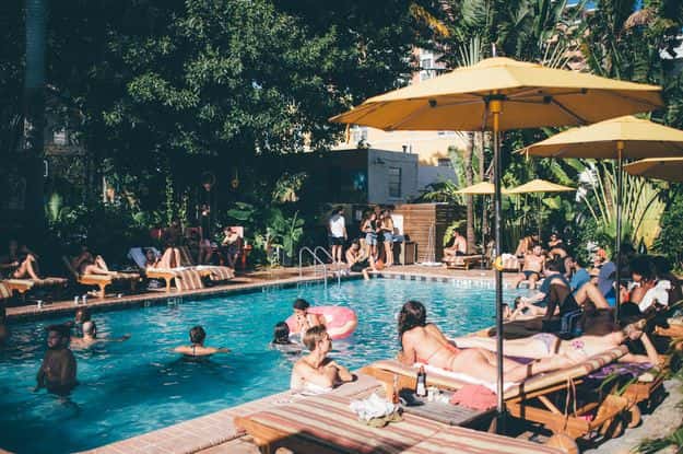 Active resort pool surrounded by guests, yellow umbrellas, lounge chairs, and tropical landscaping