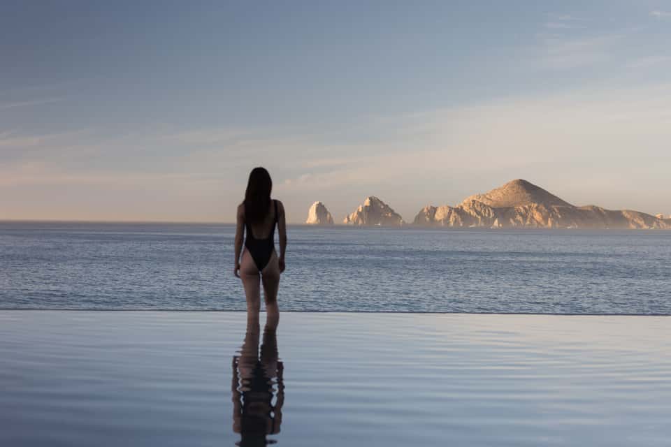 Woman in swimsuit standing in shallow water facing rocky islands and calm ocean horizon