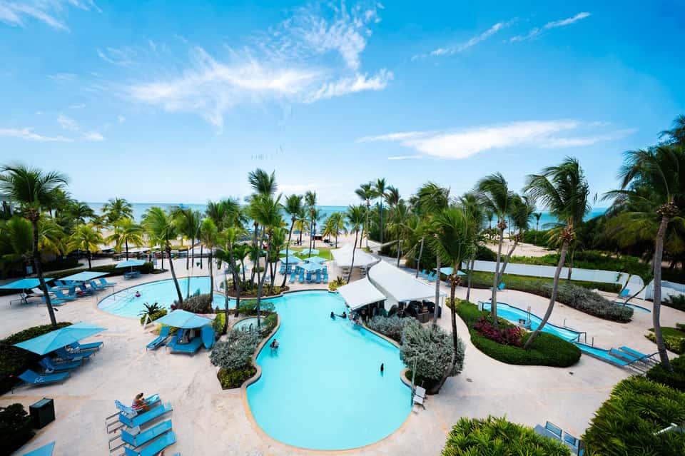 Aerial view of beachfront resort with multiple pools, palm trees, and sandy beach