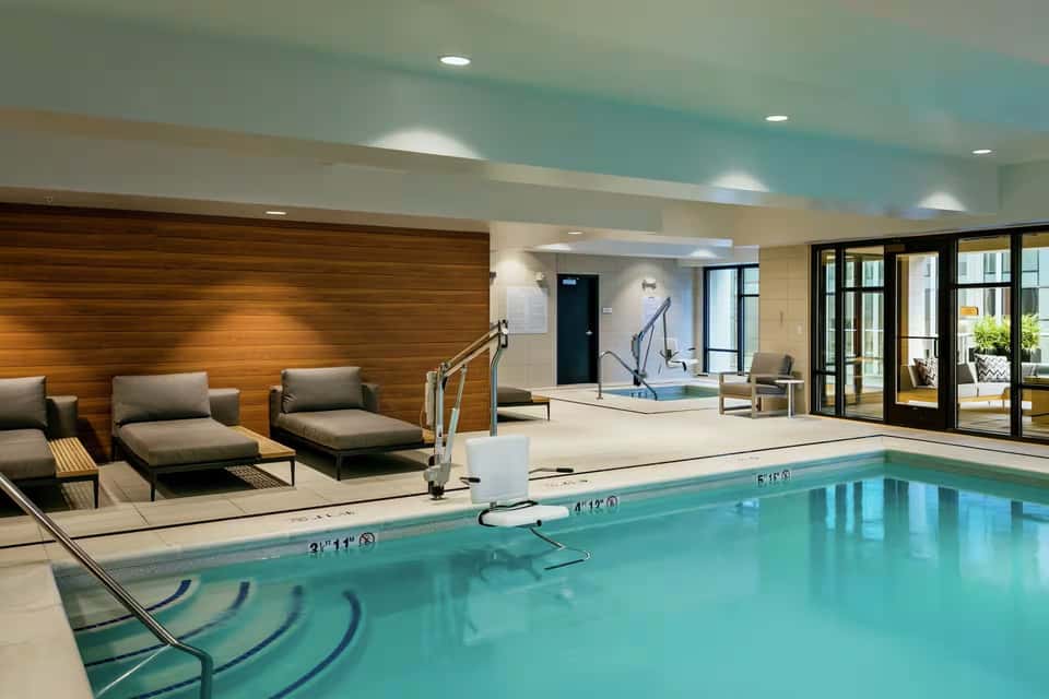 Indoor heated pool with turquoise water, wooden loungers, lounge seating area, and ceiling with teal accents