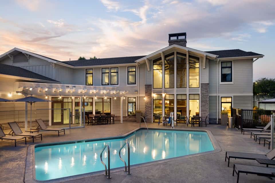 Luxury home exterior at dusk with illuminated pool, patio seating, and contemporary architecture