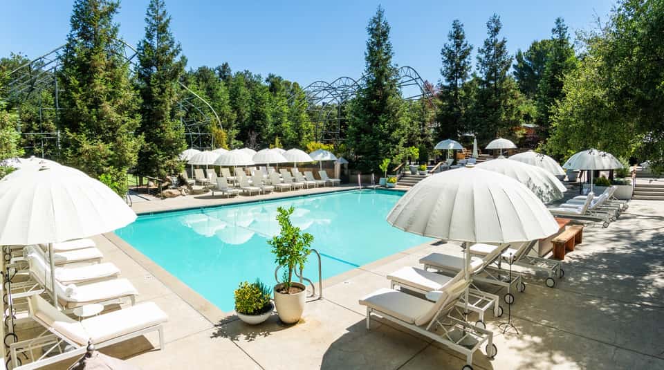 Outdoor resort pool with surrounding white umbrellas, lounge chairs, and forested landscape