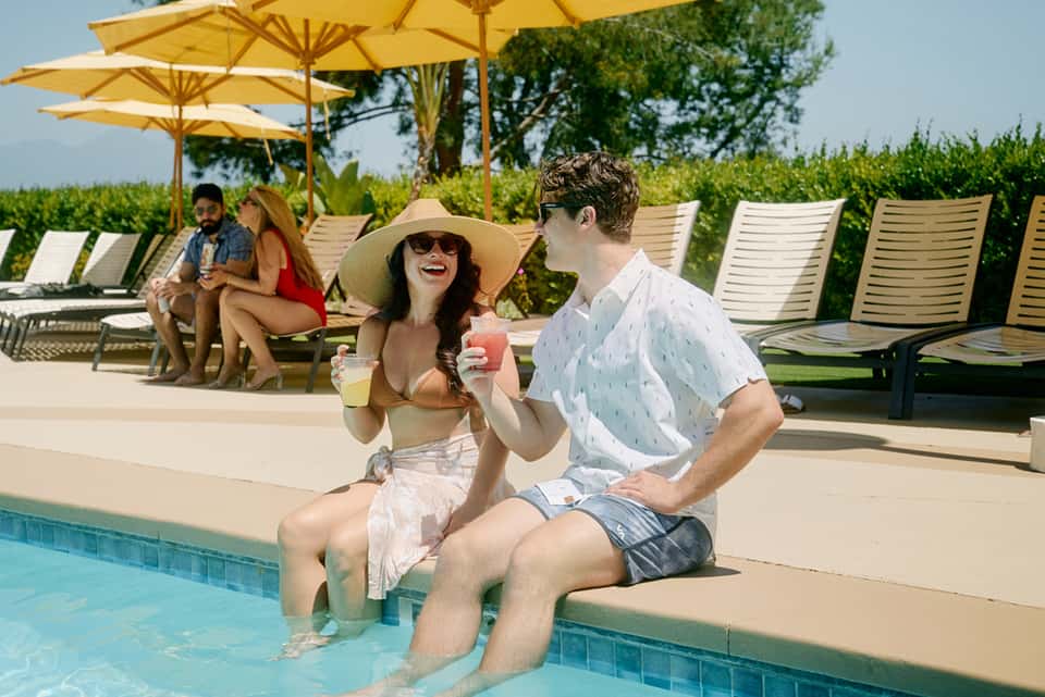 Guests sitting at pool edge with yellow umbrellas overlooking manicured lawn and hedges