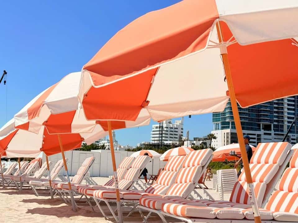 Row of red and white striped umbrellas shading beach lounge chairs with urban buildings in background