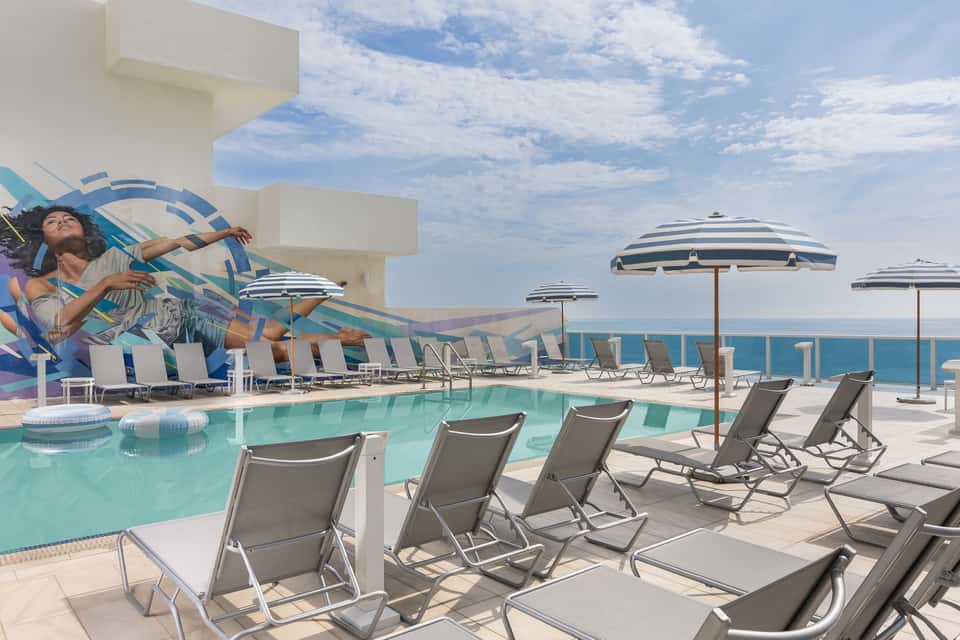 Beachfront resort pool deck with ocean views, lounge chairs, and striped umbrellas