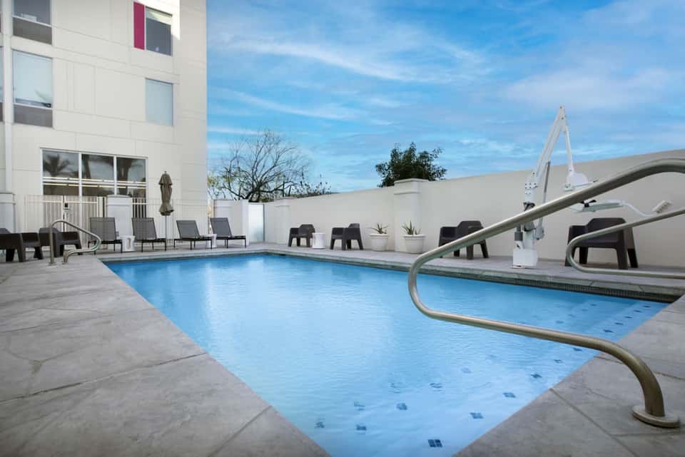 Resort pool deck during daytime with blue water, lounge chairs, umbrellas, and modern architecture