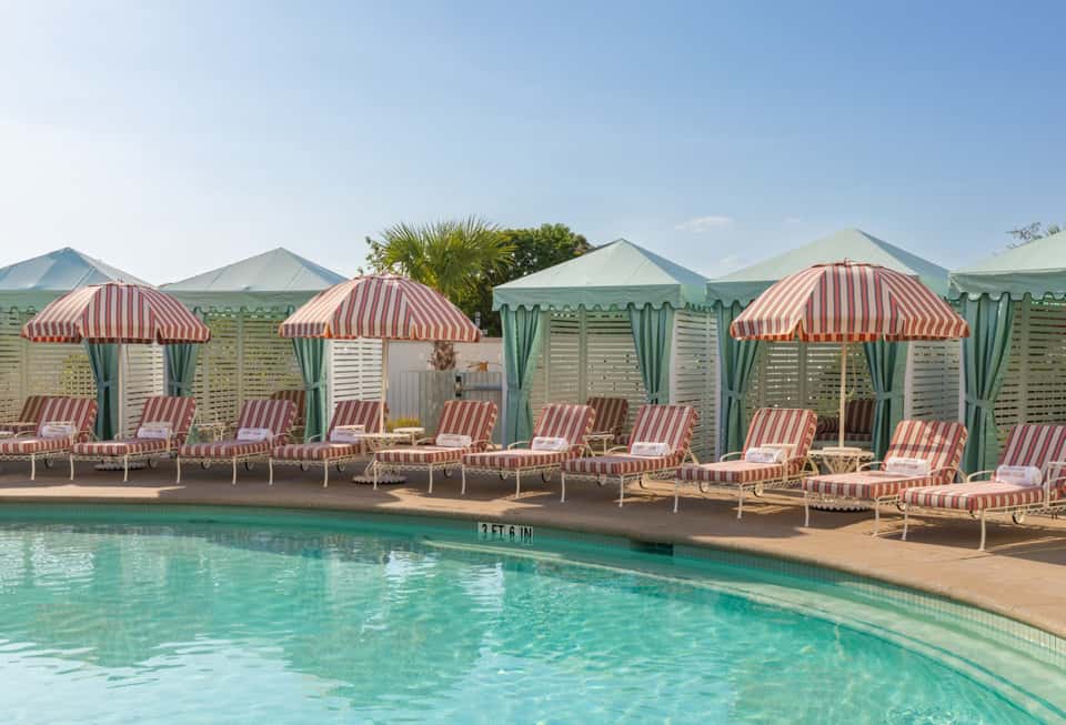 Beachfront pool area with striped red and white umbrellas, green cabanas, and turquoise water