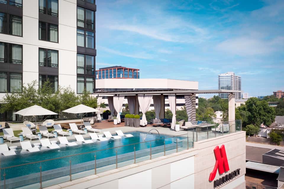 Luxury rooftop pool with lounge chairs, white umbrellas, pergola, and city skyline in background