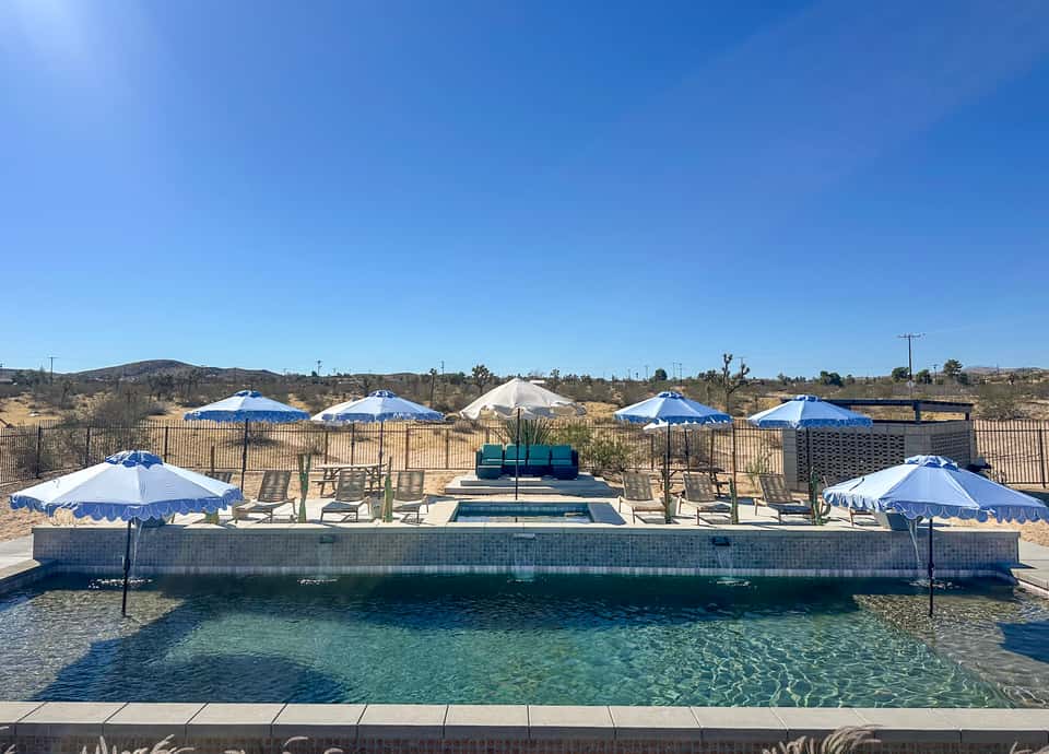 Resort pool with blue and white umbrellas, lounge chairs, and desert landscape views