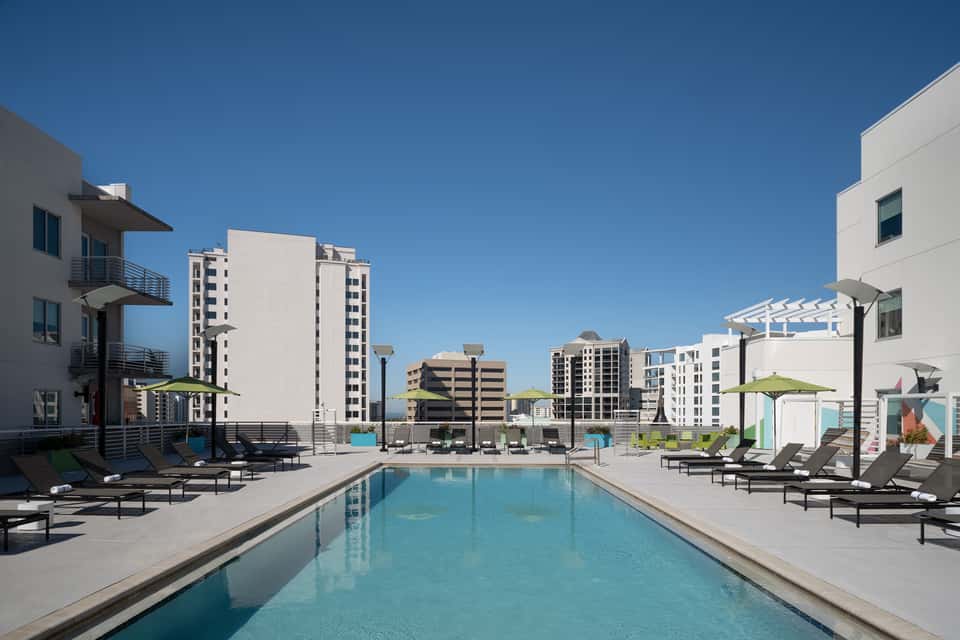 Rooftop swimming pool with lounge chairs, green umbrellas, and surrounding apartment buildings