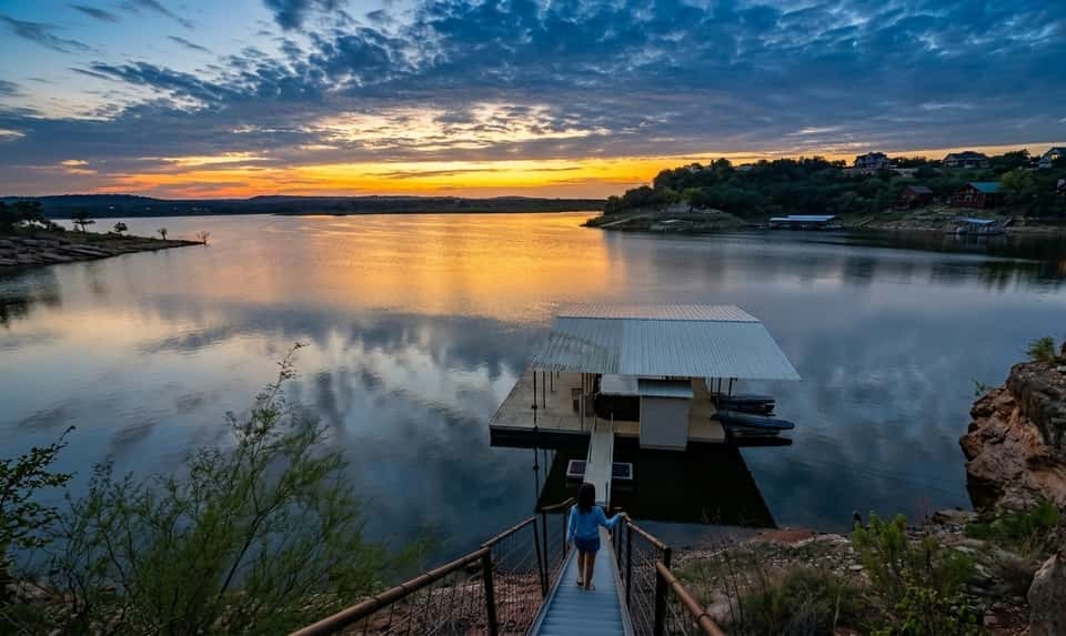 Serene sunset over a lake with a floating dock and residential area reflected in calm water