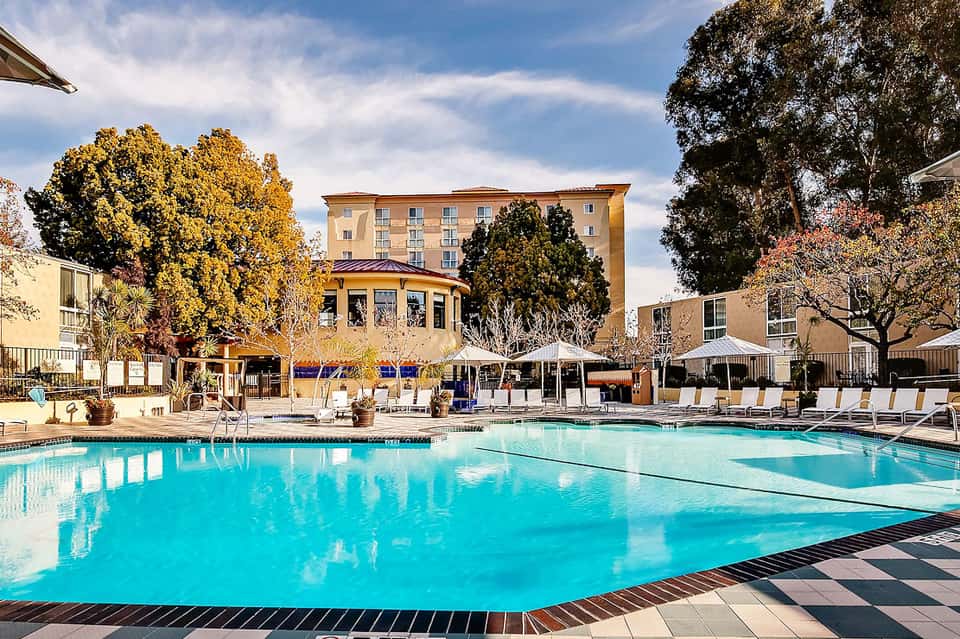 Resort pool with turquoise water, loungers, white umbrellas, and multi-story hotel building