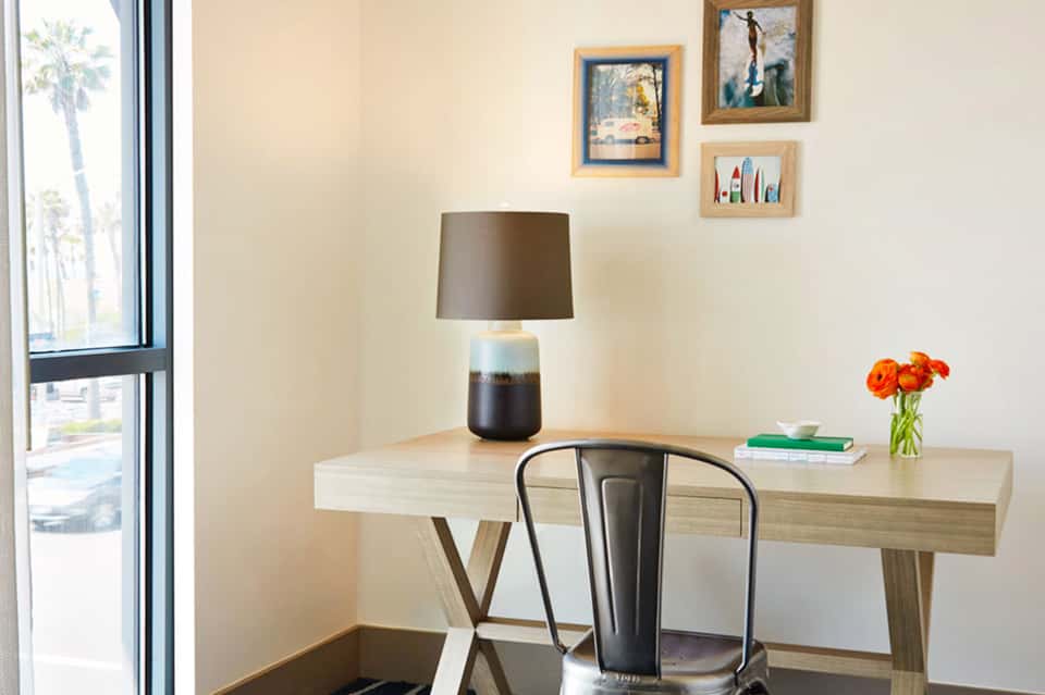 Modern hotel desk with lamp, books, and fresh flowers beside window with city view