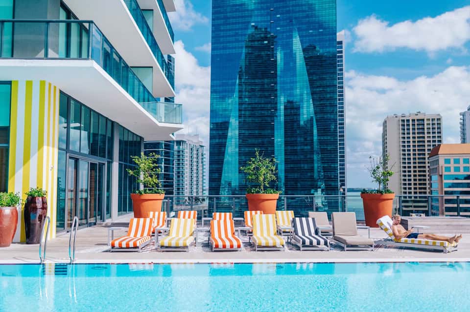 Modern rooftop pool with striped loungers overlooking city skyline and tall buildings