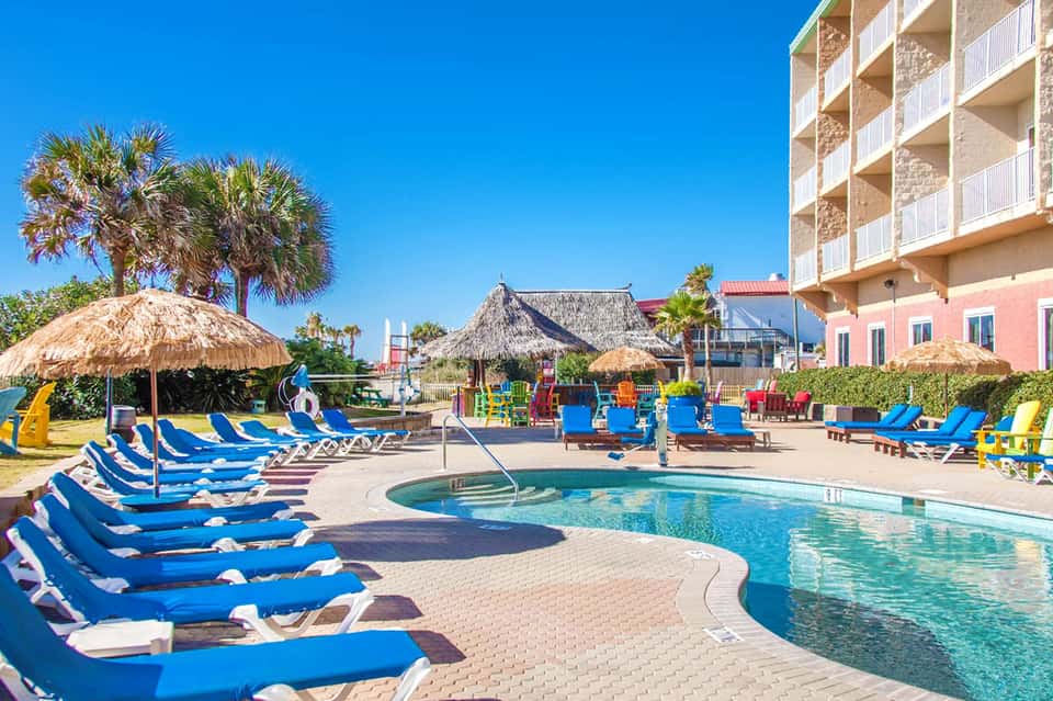 Resort pool area with blue loungers, tiki umbrellas, and colorful playground
