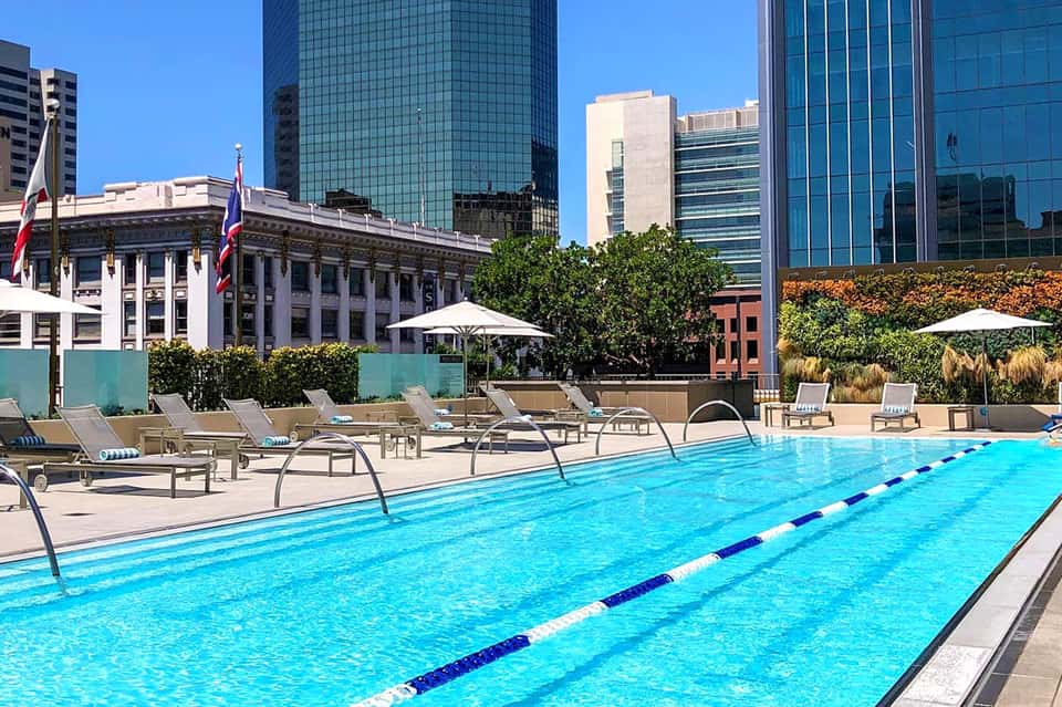 Rooftop swimming pool with lane dividers, lounge chairs, and urban skyline backdrop