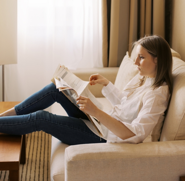 A woman relaxes on a couch, engrossed in reading a newspaper, surrounded by a warm and inviting living space.