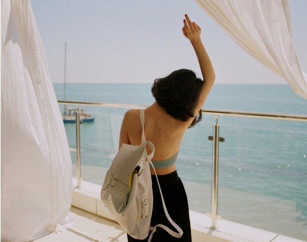 A woman wearing a white top and black skirt stands on a balcony, enjoying the scenic ocean view.