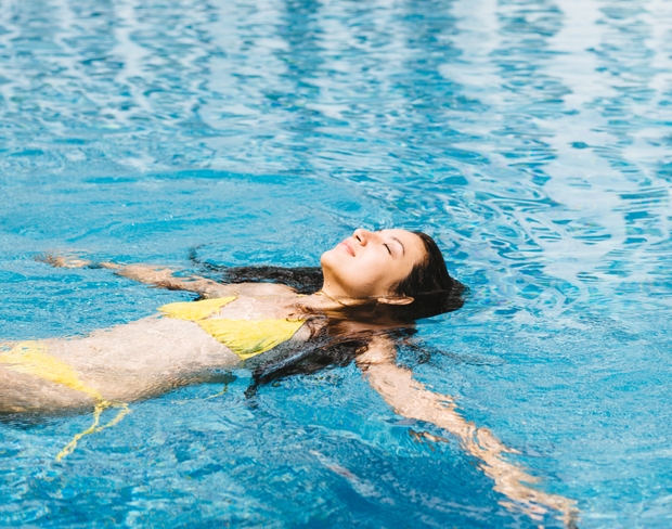 A woman wearing a yellow bikini enjoys floating in a sparkling pool on a sunny day.
