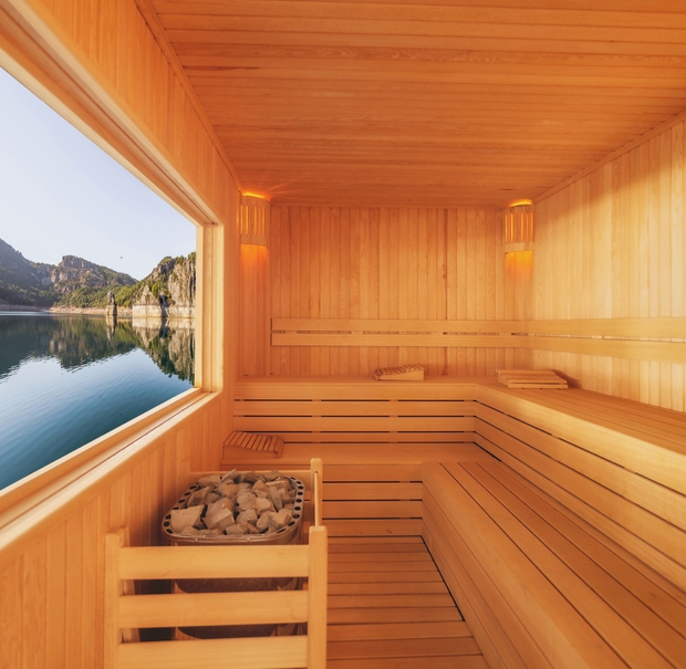 Inside a wooden sauna, large windows reveal a peaceful lake view, creating a relaxing atmosphere.
