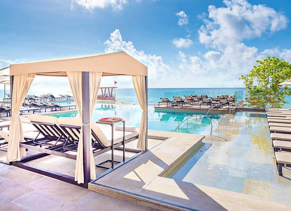 Resort's infinity pool with ocean view, lounge chairs, umbrellas, and private cabanas