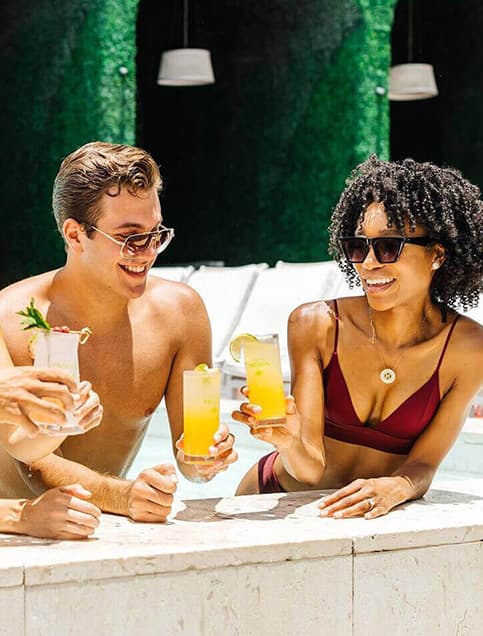 Group of friends drinking tropical cocktails by the pool at a hotel