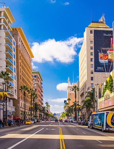Downtown street with hotels on either side and clear blue sky in the background in Los Angeles, CA